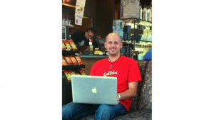 A picture of Anthony Trustee sitting in a coffee shop in his computer